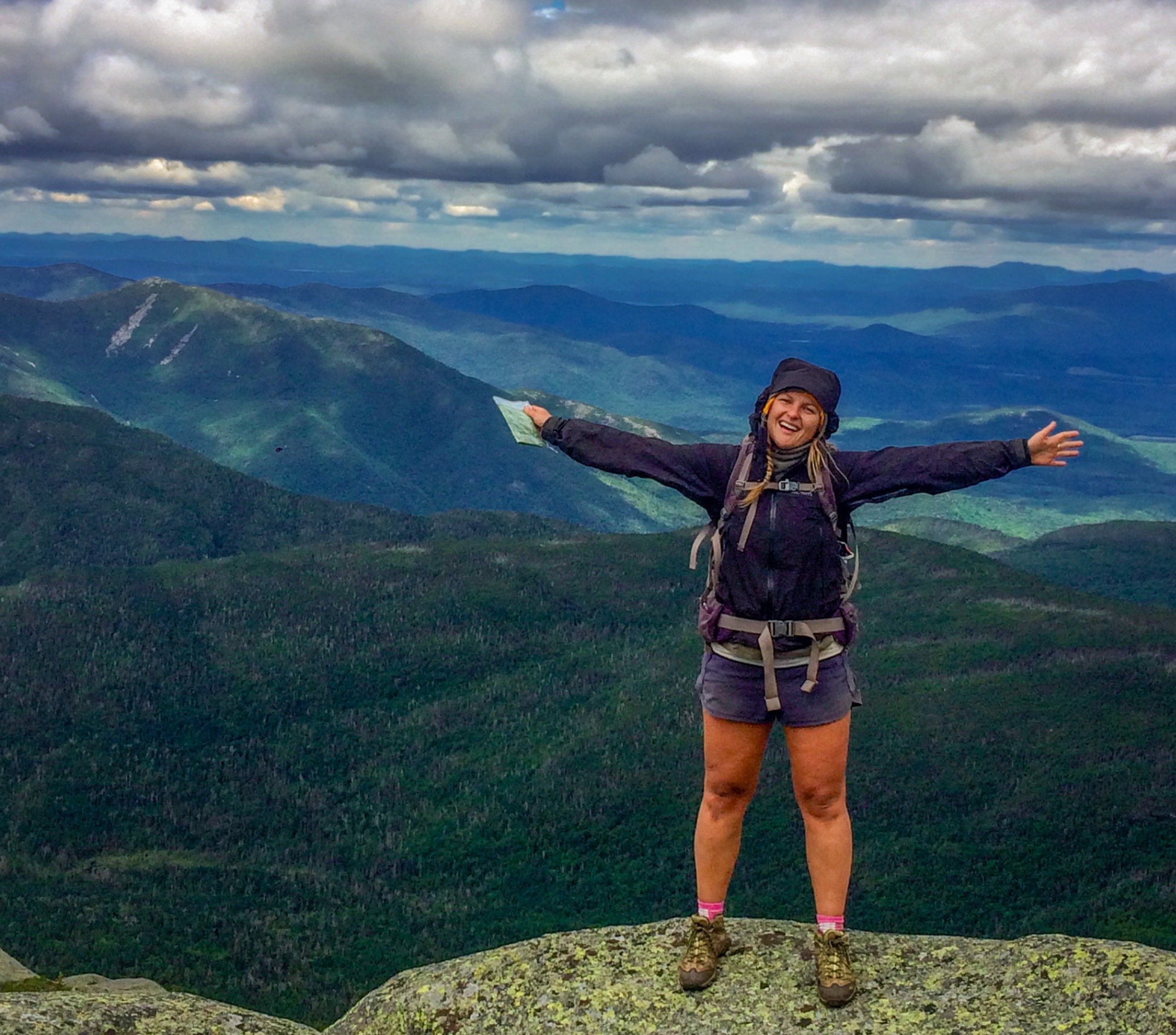 A student hiking on a mountain with their arms out wide
